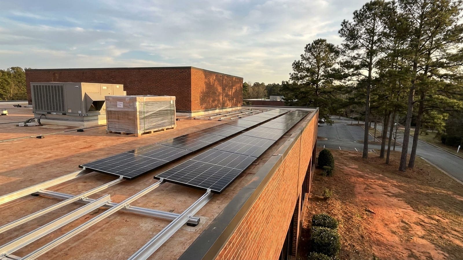 Solar modules being installed on the flat roof of a commercial building in Georgia, with racking rails and a pallet of panels waiting