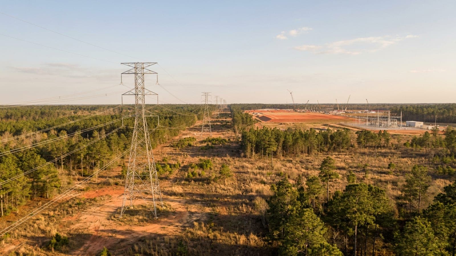 High-voltage transmission lines crossing pine flatwoods toward a new industrial campus under construction in Georgia